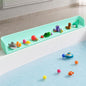 Green kids bathtub splash guard with suction cups holding bath toys on the tub edge